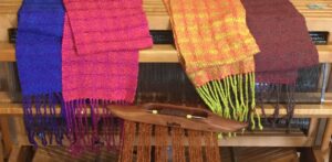 Four completed scarves draped over a loom with weaving in progress.